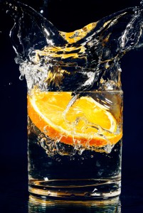 Slice of orange falling down in glass with water on deep blue
